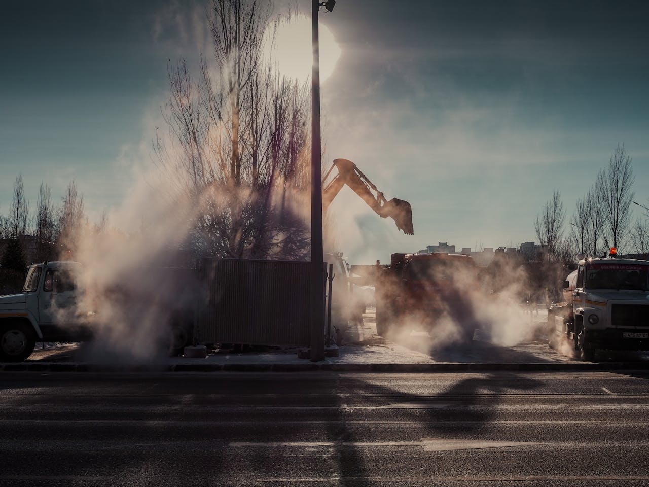why-choose-us A dramatic scene of construction work on a city street with machinery and steam at sunrise.