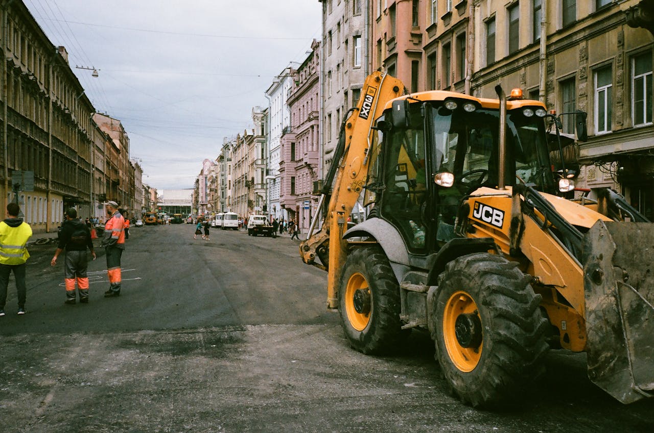 services-04 City street construction scene with workers and JCB excavator.