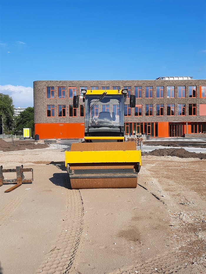 services-01 Yellow roller at construction site in front of modern building.