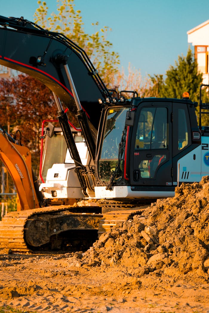 services-02 Excavator at a construction site with dirt piles and trees in background.