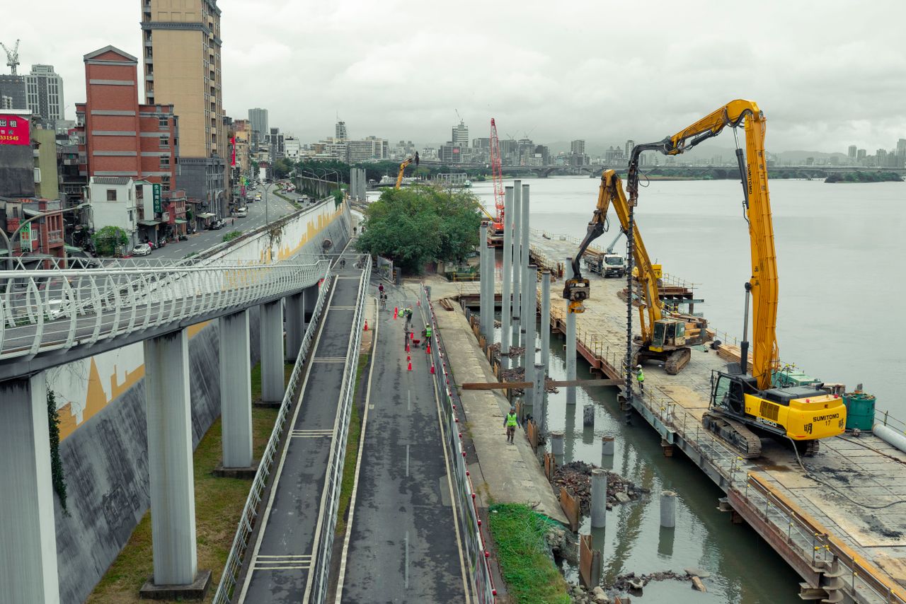 about-img Aerial view of a construction site along a riverfront in Taipei, Taiwan, with machinery and workers.